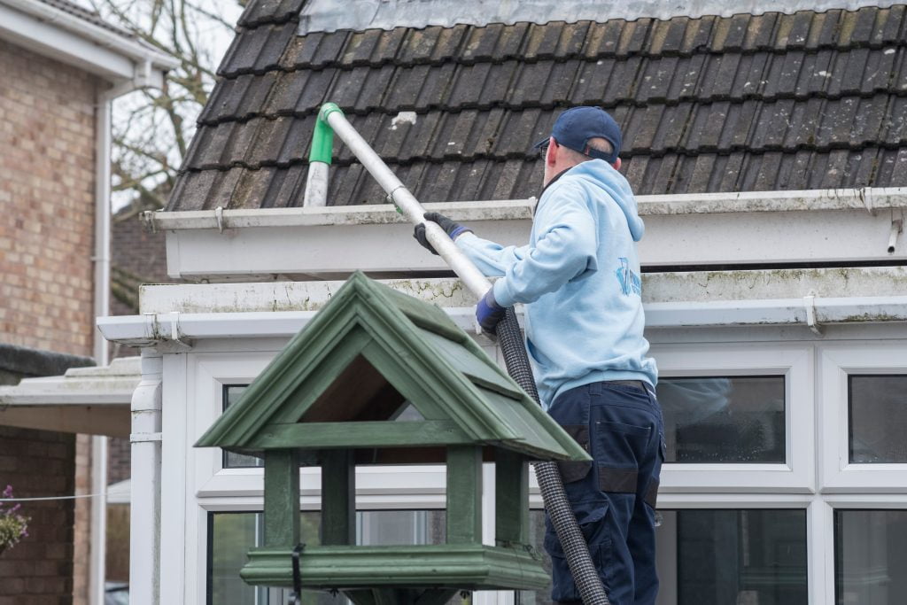 Ein Mann saugt mit einem Dachrinnensauger die Regenrinne eines Hauses frei